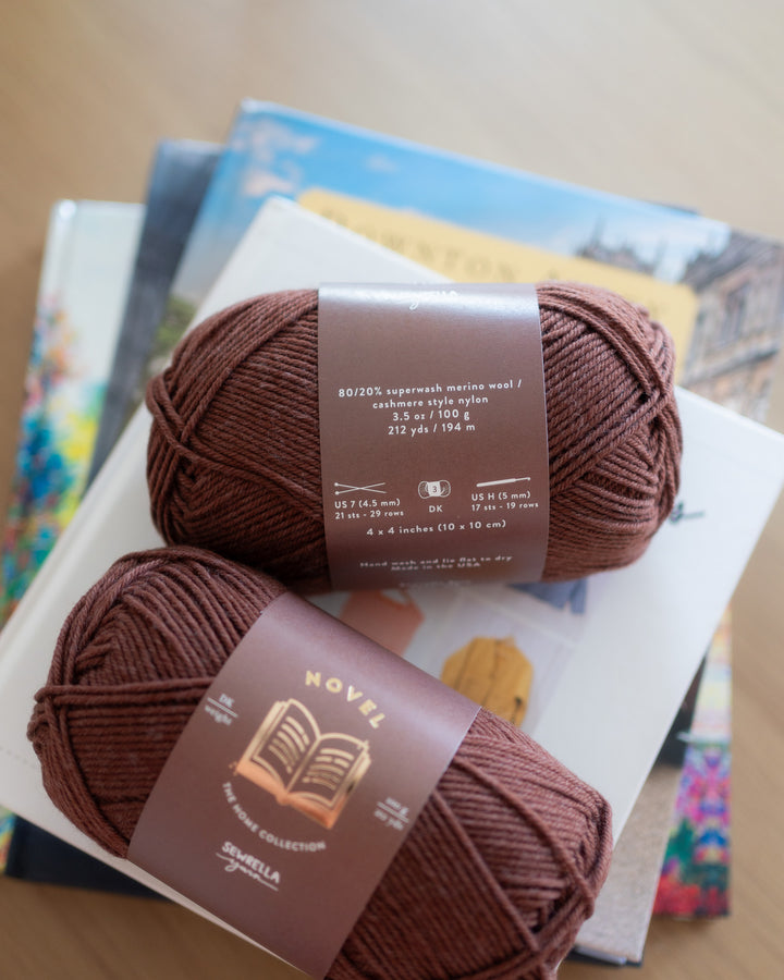 Two balls of dark brown yarn with labels on a stack of books.