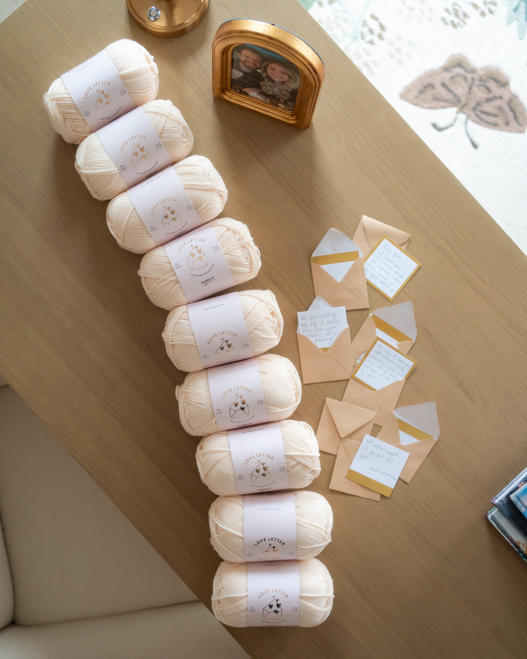 Row of white yarn balls on a wooden surface with decorative envelopes and a photo frame.