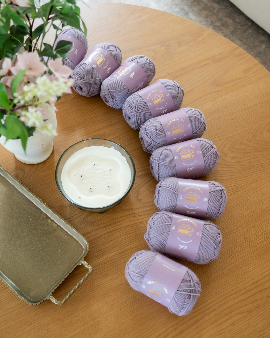 Purple yarn balls on a wooden table with a candle and flowers.