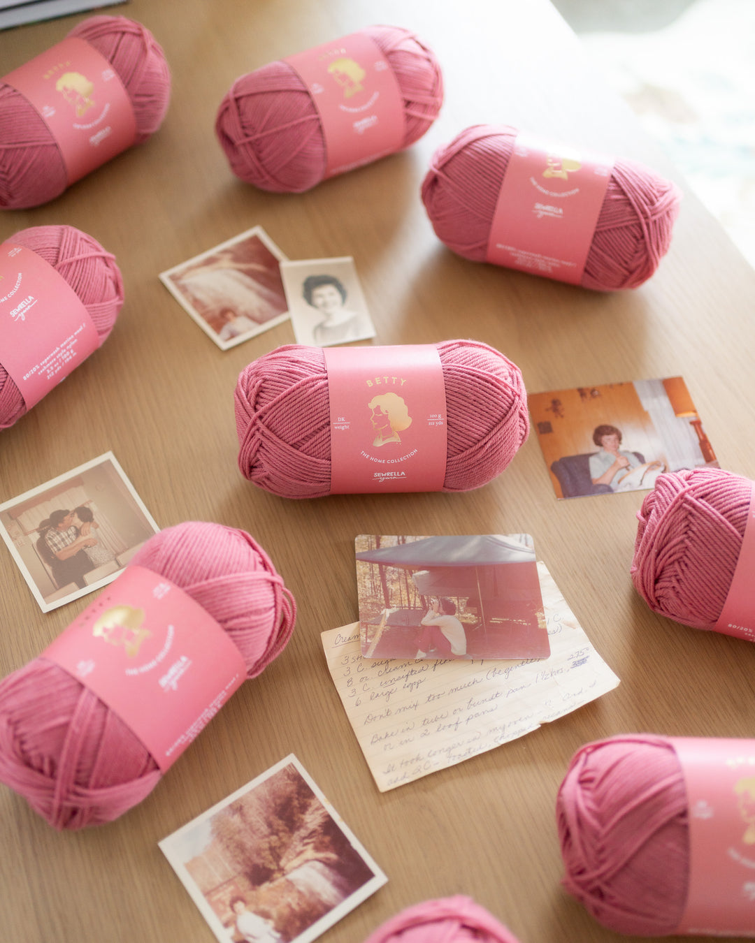 Pink yarn balls on a wooden surface with photographs underneath